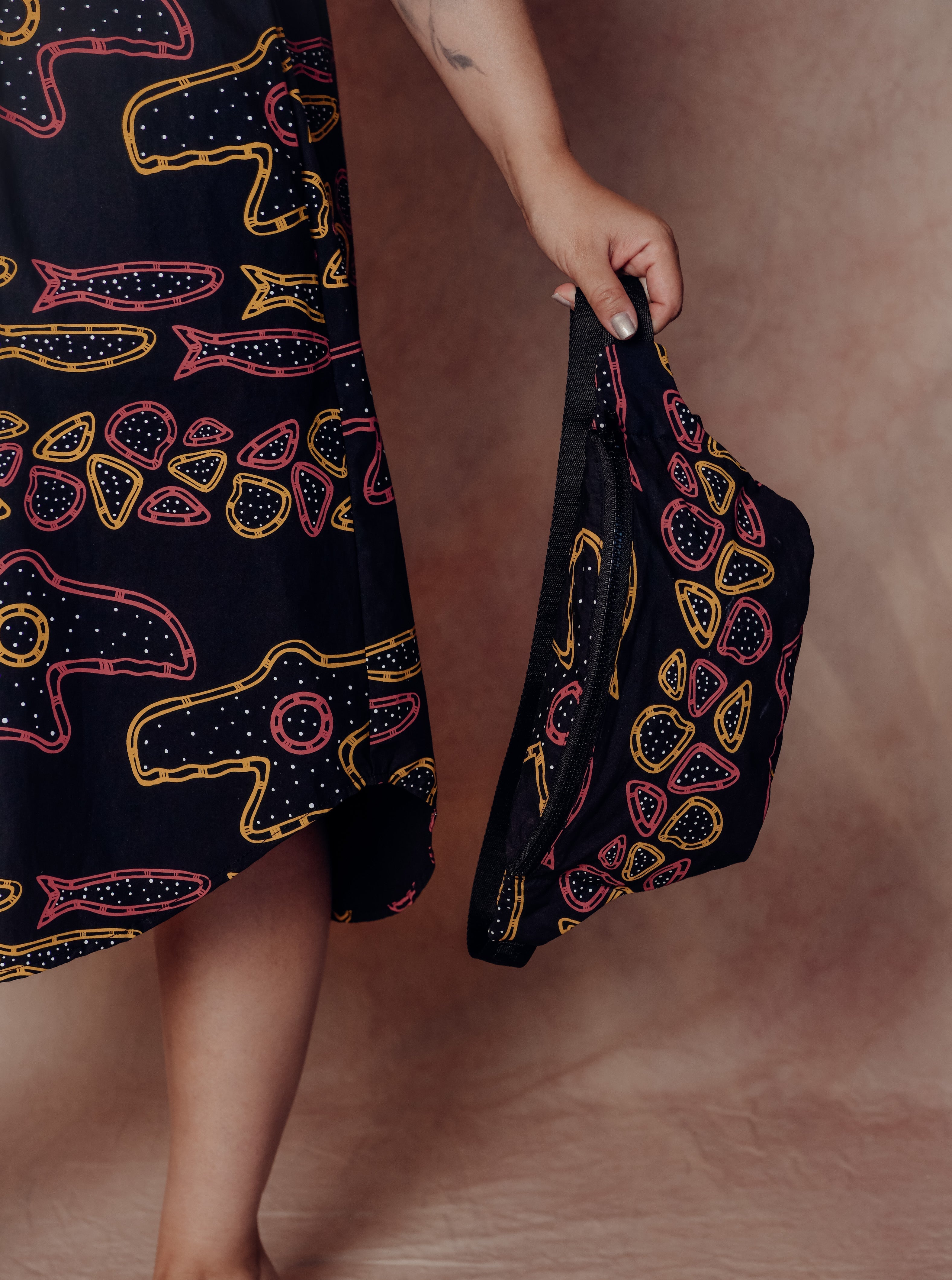 Person holding a patterned bag with a matching dress against a plain background