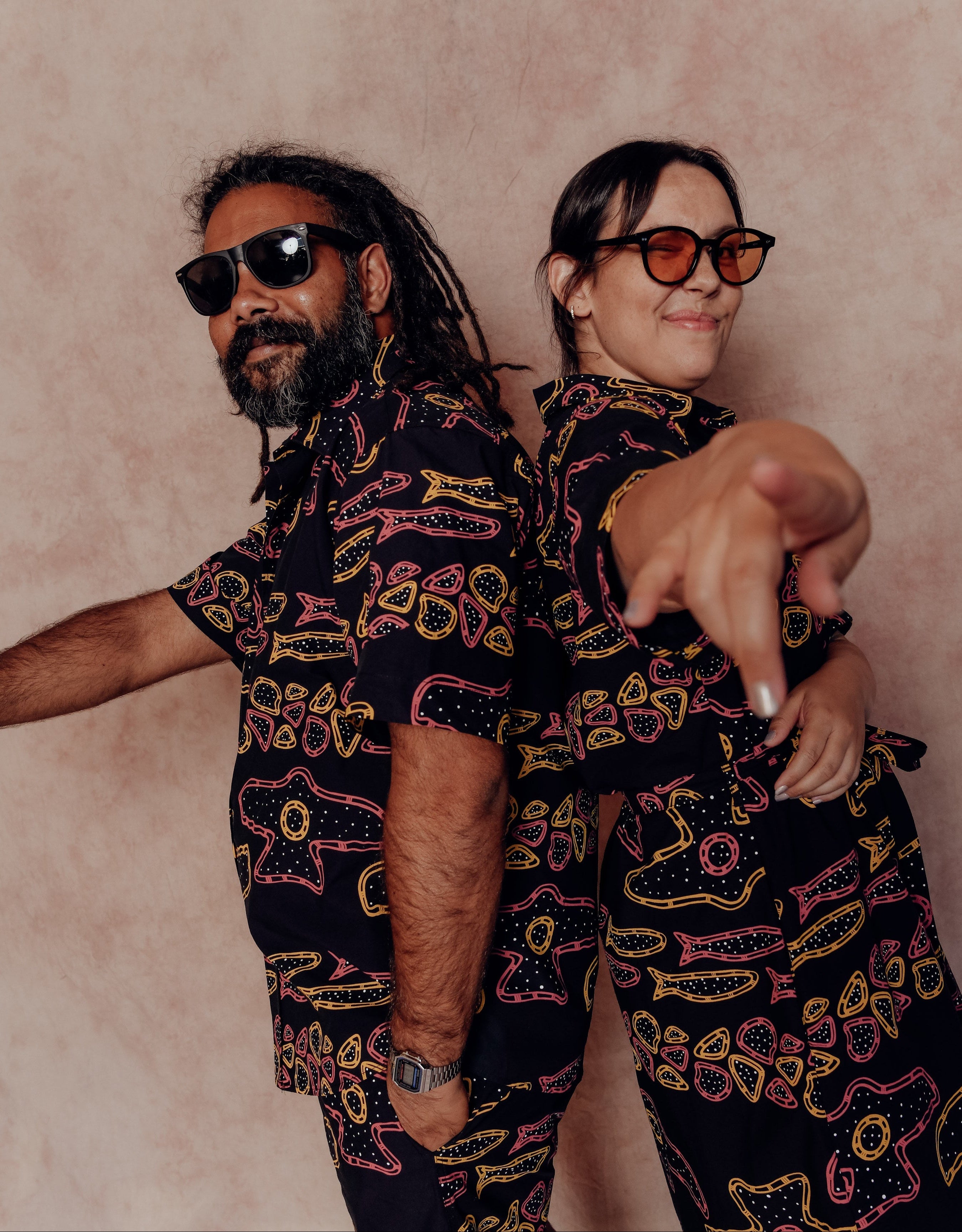 Two people wearing matching patterned outfits against a plain background